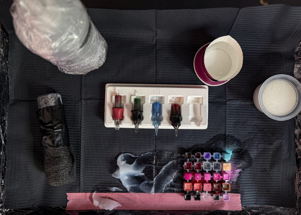 Tattoo setup with tattoo machine, wrapped green soap, vaseline, and ink caps prepared by Meow Ink Alex Lukasiewicz in Den Haag